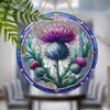 Round stained glass window hanging featuring purple and blue thistle flowers on a green stem
