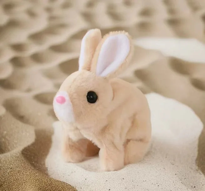 A light tan electric plush puppy toy with long ears is resting on sand.