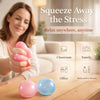 A woman squeezes a pink squishy stress relief toy on a wooden table with blue and pink balls nearby.