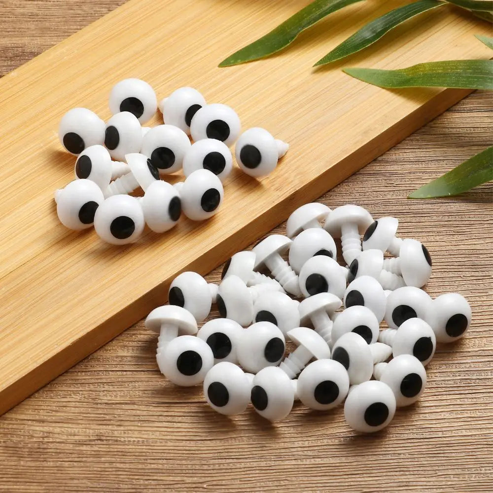 A pile of white and black plastic safety eyes for amigurumi and stuffed animals resting on a wooden board.