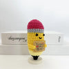 A handwoven crochet pencil ornament featuring a yellow body and a pink and gray striped cap, displayed on a white box.