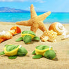 A set of twelve adorable mini sea turtle plush toys resting on sandy beach with seashells and blue ocean background.