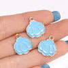 Two light blue enamel marine life charms are displayed on a hand, ready for jewelry making.