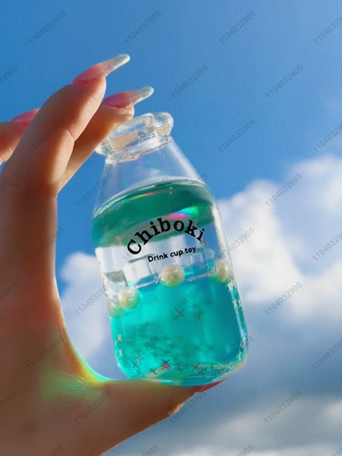 A hand holds a clear bottle filled with bright blue liquid, labeled Chiboki, against a cloudy blue sky.