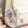 A light beige backpack features a gray dinosaur skeleton charm with a removable hood attached to the zipper pull.