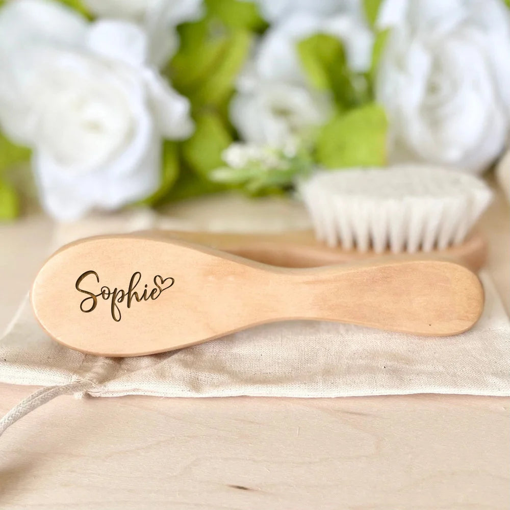 A light wooden baby brush and comb set with the name Sophie engraved on the handle, resting on a beige cloth.