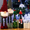 A festive Christmas doll dress-up set featuring knitted hats and scarves displayed next to a decorated Christmas tree.