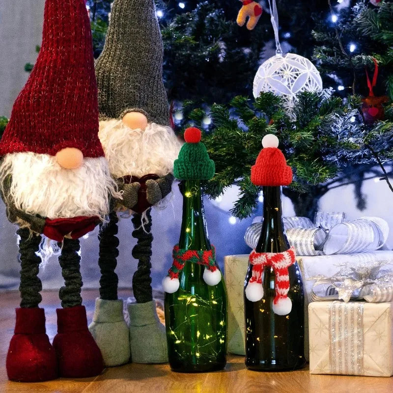 A festive Christmas doll dress-up set featuring knitted hats and scarves displayed next to a decorated Christmas tree.