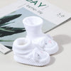 A pair of white handmade knitted baby booties with non-slip soles displayed on a book.