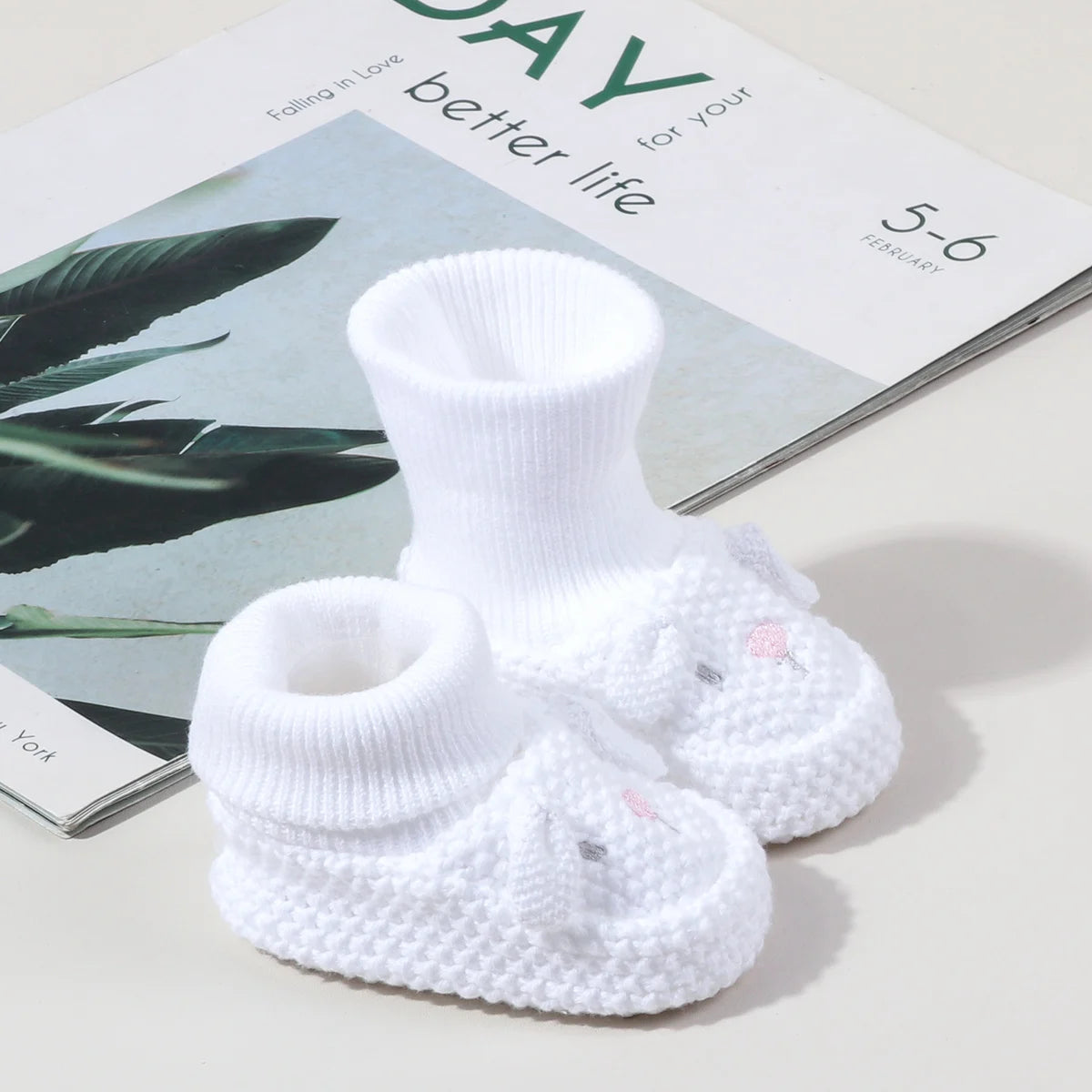 A pair of white handmade knitted baby booties with non-slip soles displayed on a book.