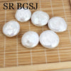 A collection of smooth, round natural white freshwater pearl beads arranged on a light wooden surface.