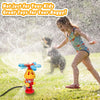 A woman is spraying water from a cartoon fire hydrant toy toward a dog in a grassy outdoor setting.