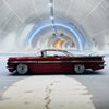 A red vintage 1959 Chevrolet Impala die-cast model car is photographed inside a futuristic, arched tunnel.
