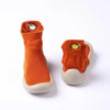 A pair of orange baby first walker socks with a yellow fish design on the toe and a light gray sole.