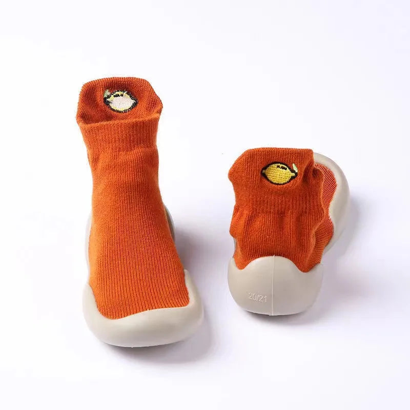 A pair of orange baby first walker socks with a yellow fish design on the toe, shown against a white background.