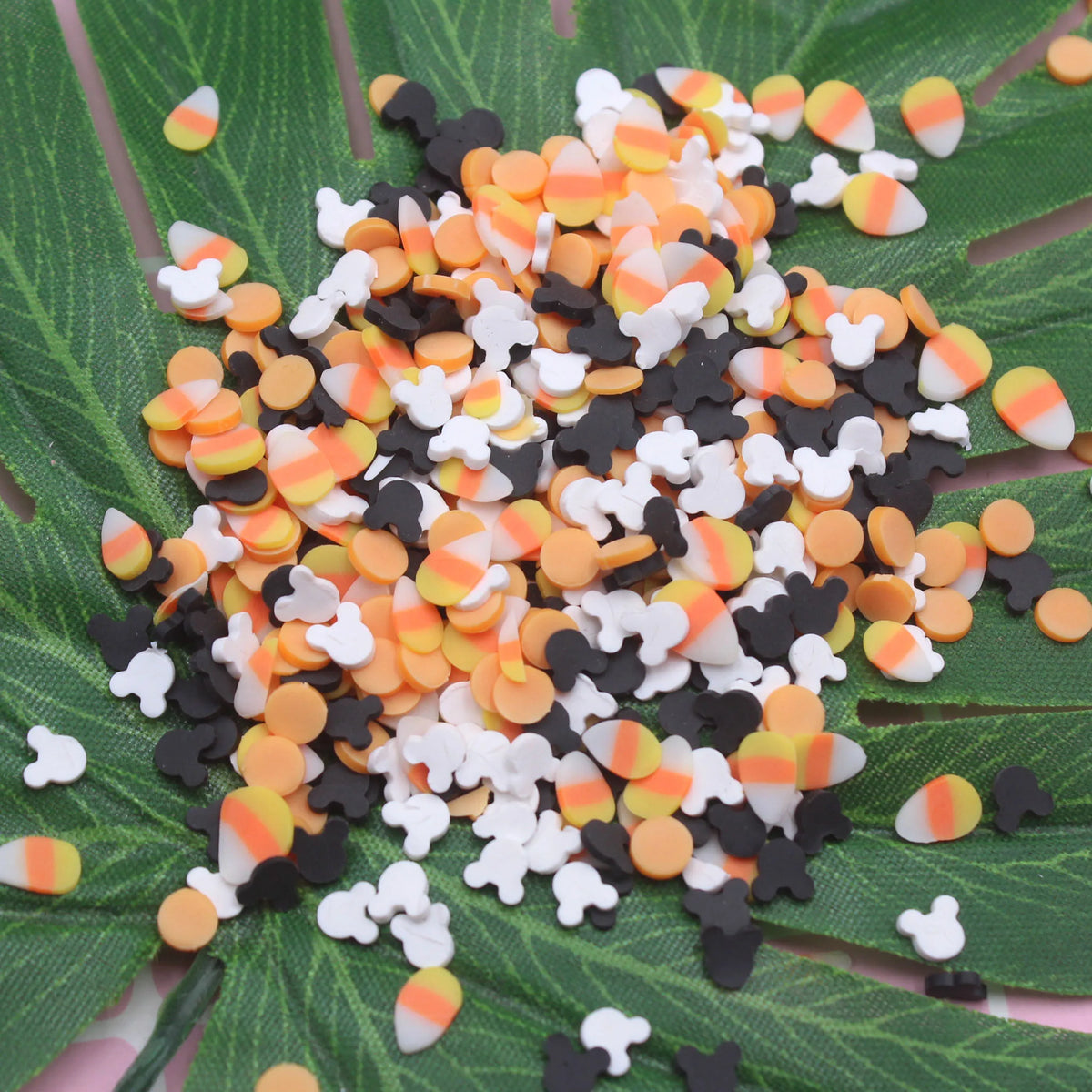 A pile of small, round polymer clay slices in black, white, and orange stripes scattered on a green leaf.