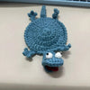 A handmade crochet lizard coaster in blue with a funny expression.