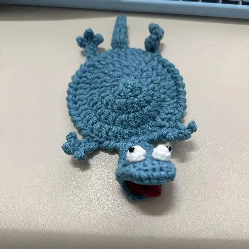 A handmade crochet lizard coaster in blue with a funny expression.