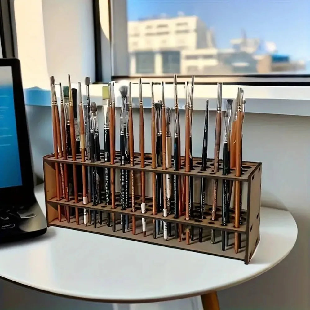 A wooden organizer holding numerous art brushes and pencils arranged in slots on a white table.