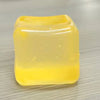 Un cube jouet squishy jaune translucide et carré posé sur une surface claire.
