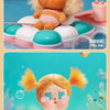 A pink and orange vinyl figure of a girl with blonde hair is shown in a bathtub setting.