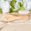 A light wooden baby brush and comb set with the name Amelia engraved on the handle, resting on a beige cloth.