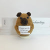A handwoven crochet ornament shaped like a brown pig with dark ears and eyes, sitting on a white base.