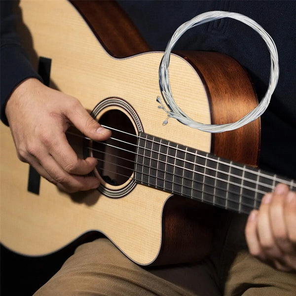 A hand plays a light-colored acoustic guitar with silver-plated nylon strings.