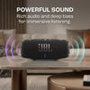 A black JBL speaker is placed on a wooden table with sound waves emanating from it.