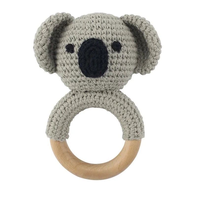 A gray knitted elephant rattle and teether ring made of soft yarn attached to a wooden loop.