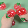 A hand holds a bright red squishy tomato stress relief fidget toy against a green background.