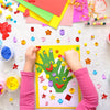 A child's hands are placing colorful acrylic gems and stickers onto a yellow craft sheet.