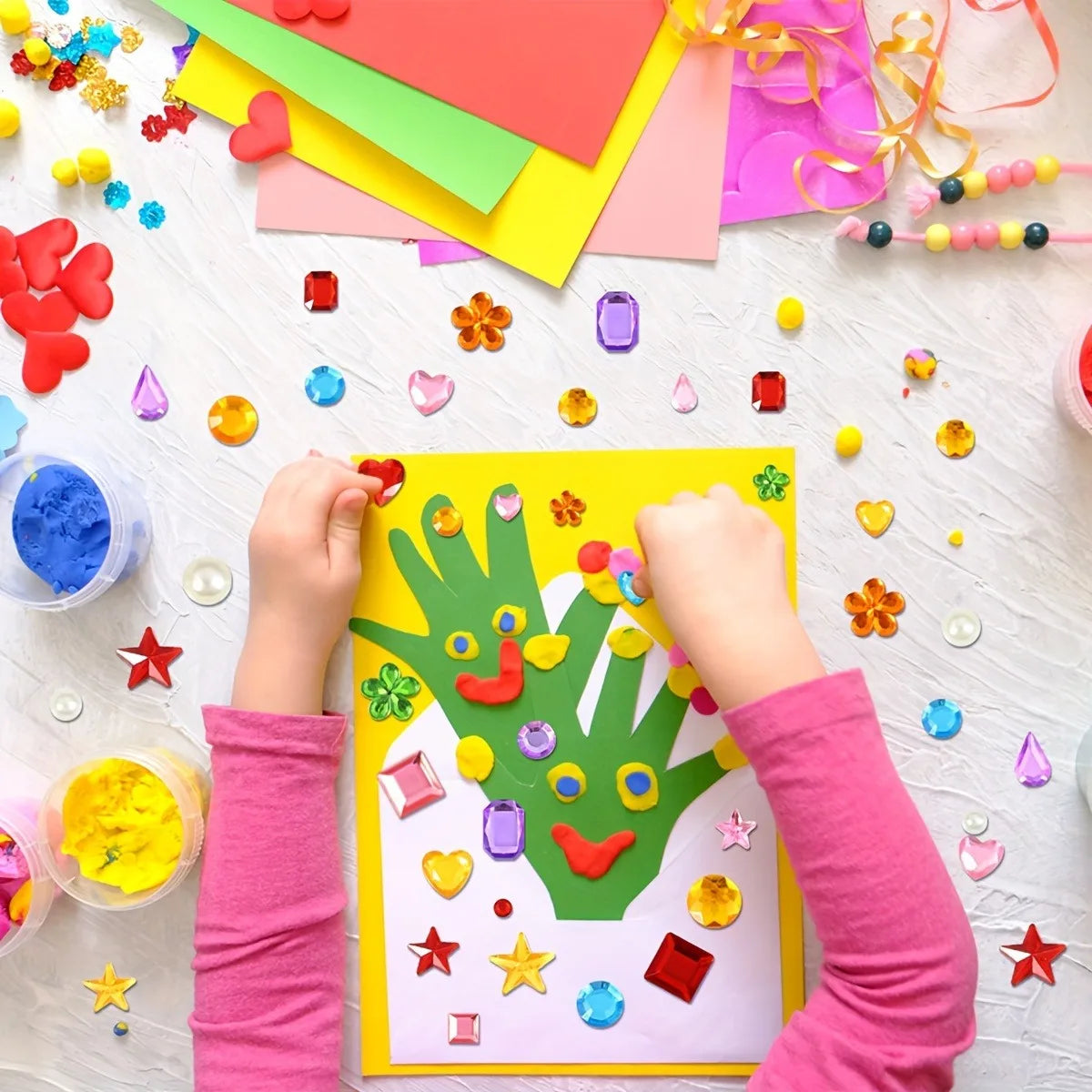 A child's hands are placing colorful acrylic gems and stickers onto a yellow craft sheet.