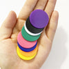 A hand holds a stack of colorful plastic game markers in various shades of purple, green, black, white, pink, blue, and yello