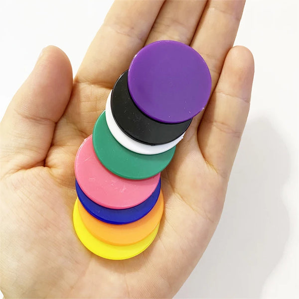 Une main tient une pile de pions de jeu en plastique multicolores dans des tons de violet, vert, noir, blanc, rose, bleu et j
