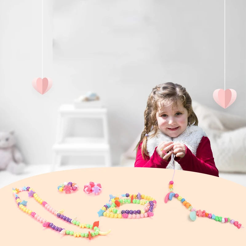 A collection of colorful bead jewelry kits and strings laid out on a light pink surface.