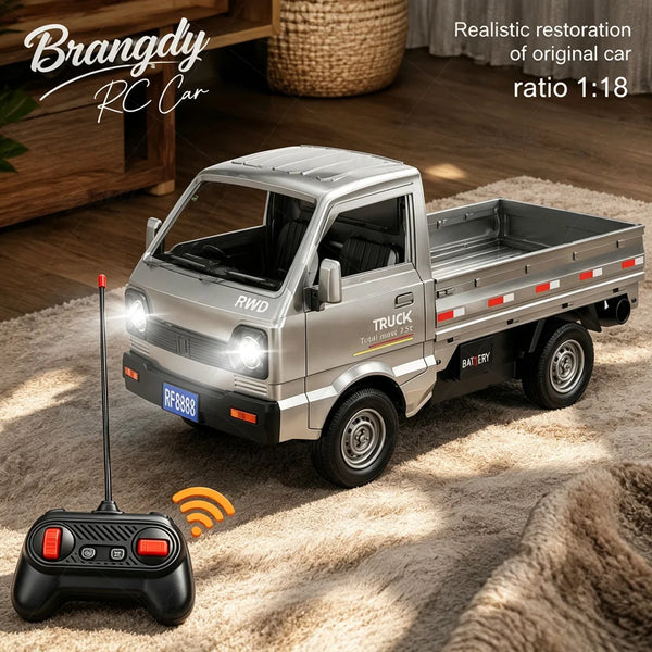 Ein silbernes RC-Truckmodell auf einem Teppich neben der Fernbedienung, im Hintergrund eine Holzkiste.