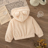 A cream-colored, knitted plush hooded winter jacket for a baby girl is displayed on a wooden surface.