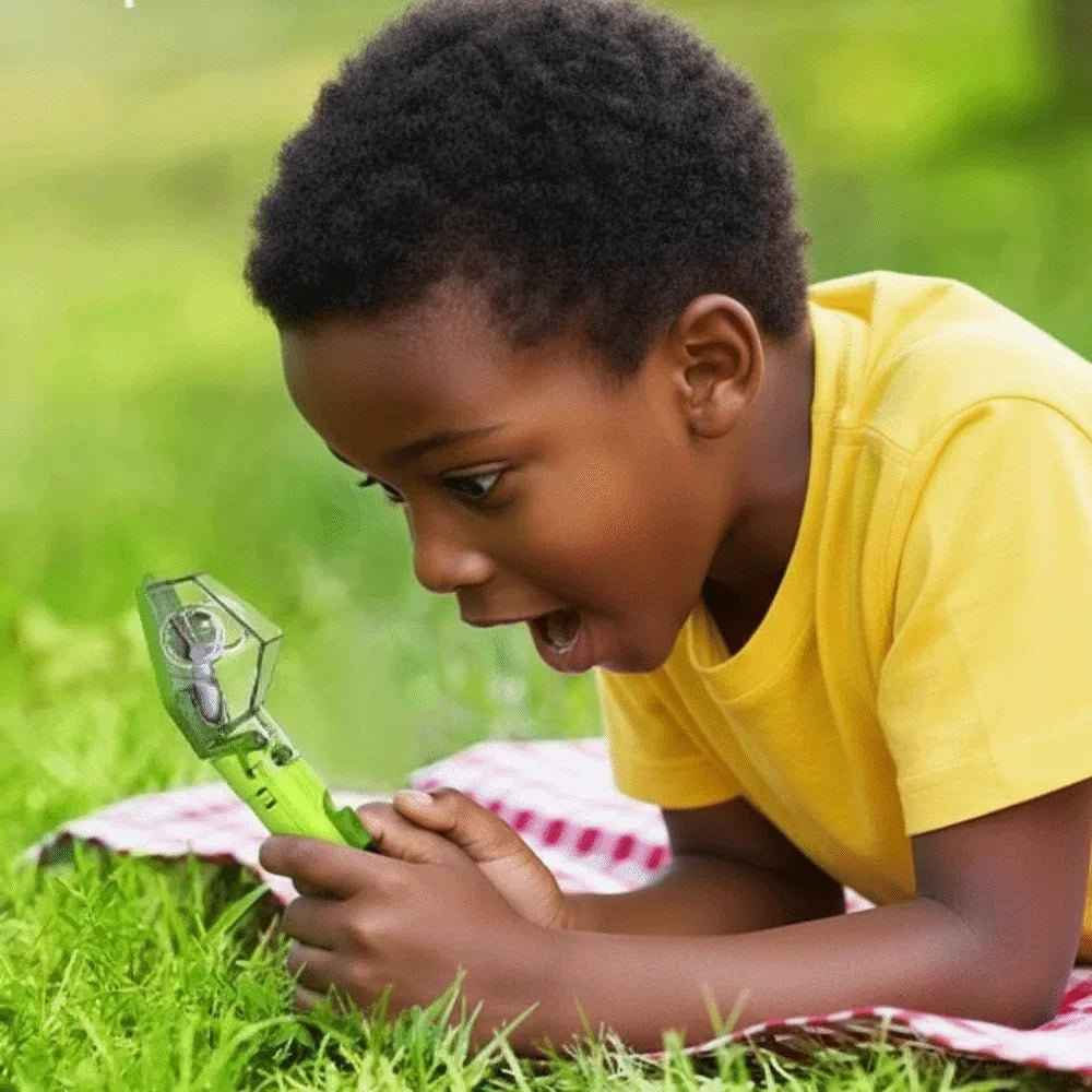 A young child is holding a green handheld insect catcher outdoors on the grass.
