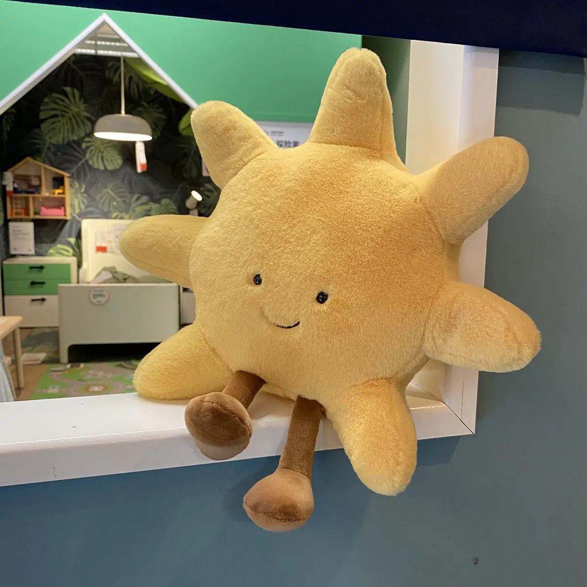 A yellow sun plushie with a smiling face and brown limbs is displayed on a white shelf.