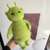 A hand holds a bright lime green alien cat plush toy with large eyes and small green horns.
