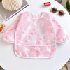 A pink full-sleeve waterproof baby bib featuring a cute cartoon rabbit design placed on a white table.
