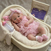 A realistic soft silicone reborn baby doll with a pink outfit is displayed in a wooden box.
