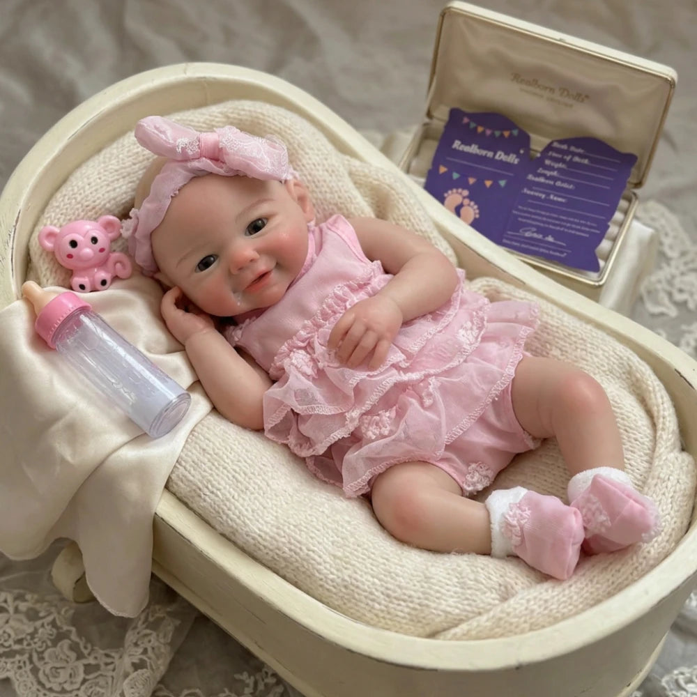 A realistic soft silicone reborn baby doll with a pink outfit is displayed in a wooden box.