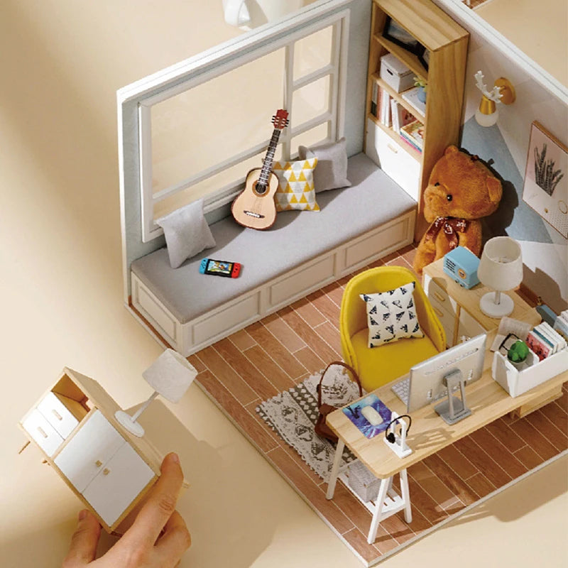 A DIY wooden miniature dollhouse kit is displayed on a wooden shelf next to a window frame.