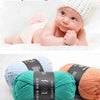 A baby is shown next to a ball of bright green milk cotton yarn and a wooden ruler.