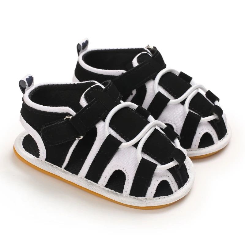 A pair of black and white breathable baby first walker sandals with a soft anti-slip sole.