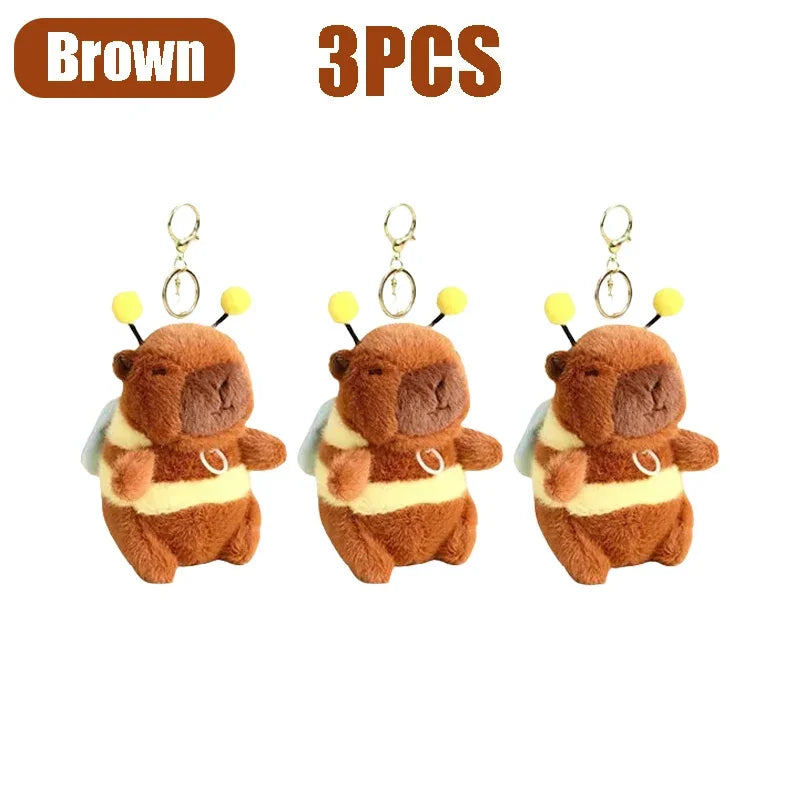 Three brown capybara plush toys with gold-colored keychains and yellow accents