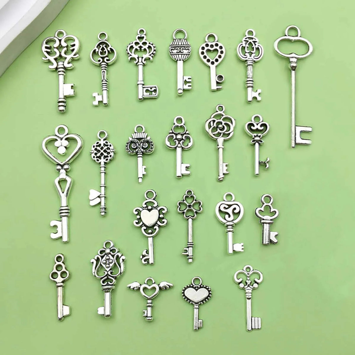 A collection of vintage key charms and pendants in silver metal on a light green background.