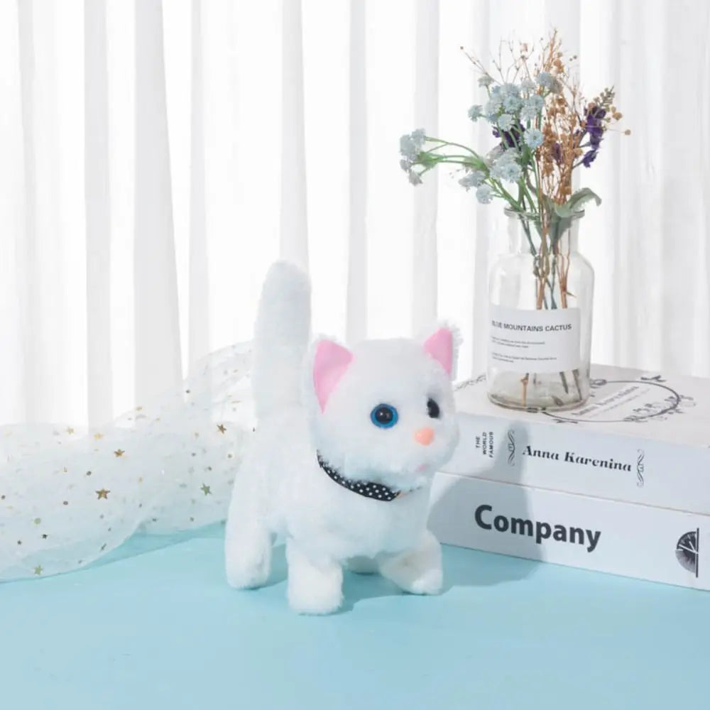 A white plush cat toy with pink ears and blue eyes sitting on a light blue surface next to a glass vase of dried flowers.